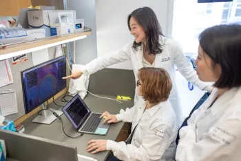 Carissa chu points to computer screen working with lab researchers